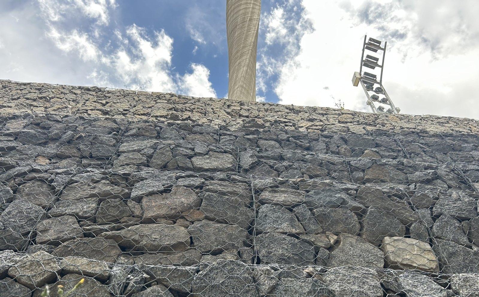 Gabion wall seen from below, with the Faro del Bicentenario in the background against the sky